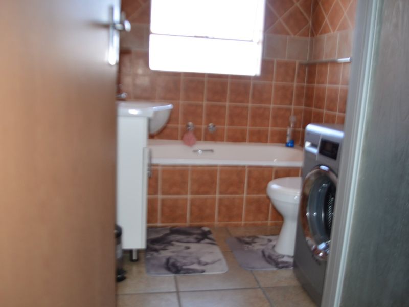 A functional bathroom featuring a built-in bathtub, pedestal basin, and toilet with classic brown wall tiling.