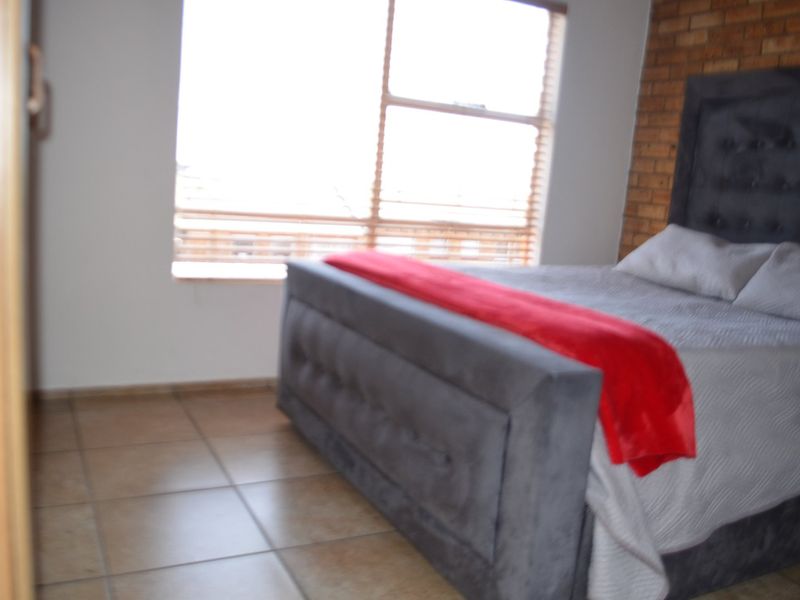 A bedroom featuring an exposed brick accent wall, tiled flooring, and a large window that allows for natural light.
