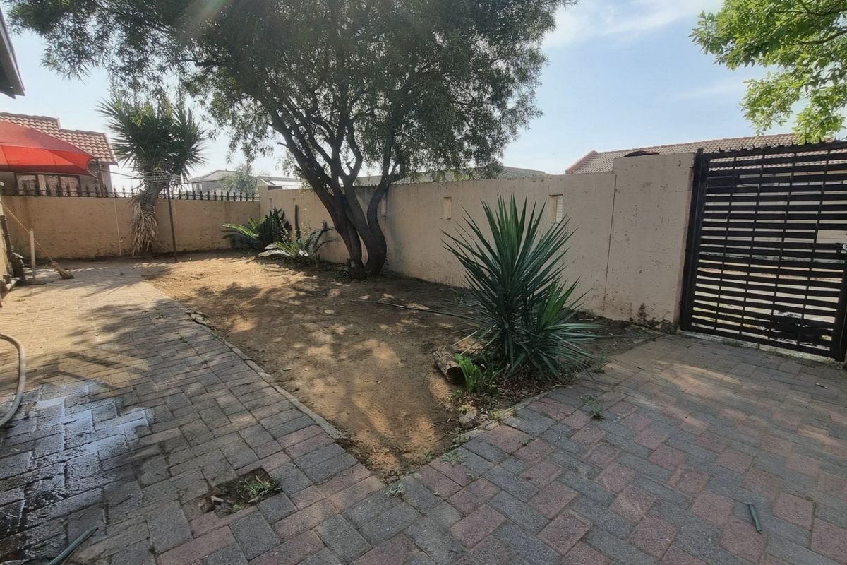 A rear garden area featuring a paved patio, perimeter walling, and a metal gate, offering potential for landscaping and outdoor improvement.