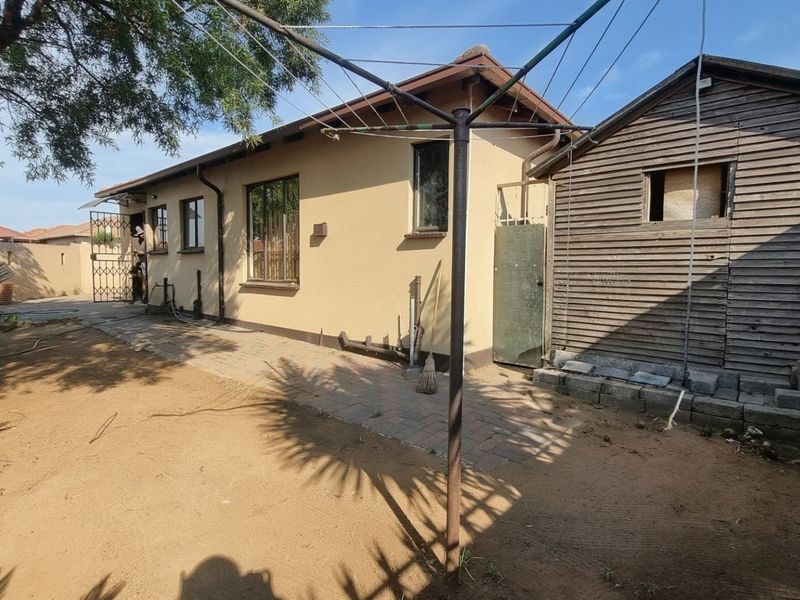 Rear exterior view of the property featuring a paved walkway, a timber storage shed, and security features on windows and doors.