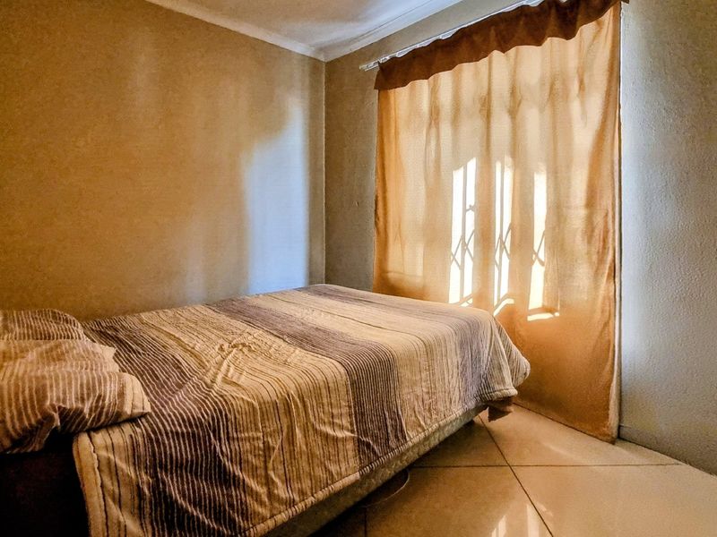 A standard bedroom featuring tiled flooring and a window fitted with a security gate, providing a functional and private sleeping space.