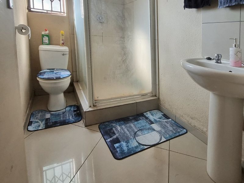 A functional bathroom featuring a pedestal basin, a shower enclosure, and a toilet, with tiled flooring and security bars on the window.