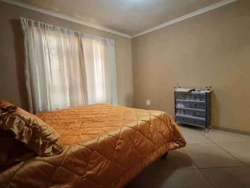 A simple bedroom featuring tiled flooring and neutral wall finishes, providing a functional space with natural light from the window.