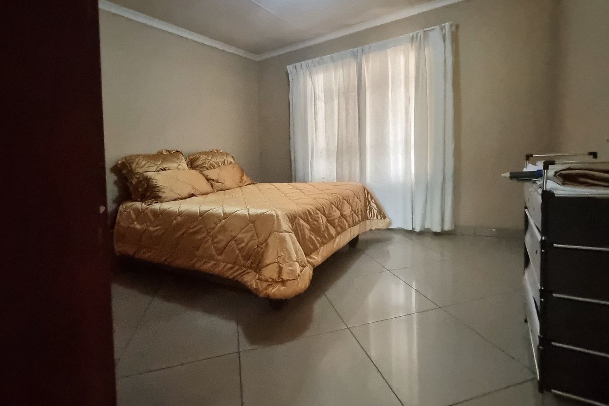 A simple bedroom featuring tiled flooring and neutral wall tones, offering a functional space with natural light through the window.