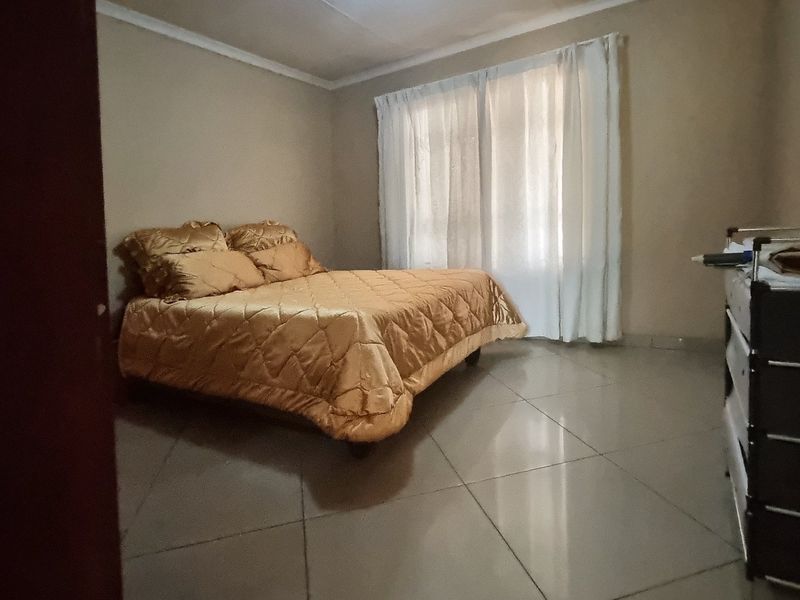 A simple bedroom featuring tiled flooring and neutral wall tones, offering a functional space with natural light through the window.