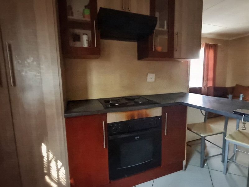 Compact kitchen featuring built-in oven, electric hob, extractor fan, and a breakfast bar, showing signs of wear and heat damage to cabinetry.