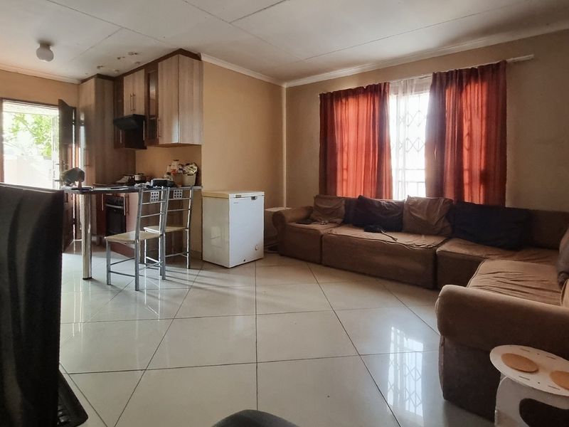Open-plan living and kitchen area featuring tiled flooring, built-in cabinetry, and an extractor fan, offering a functional layout with potential for cosmetic updates.