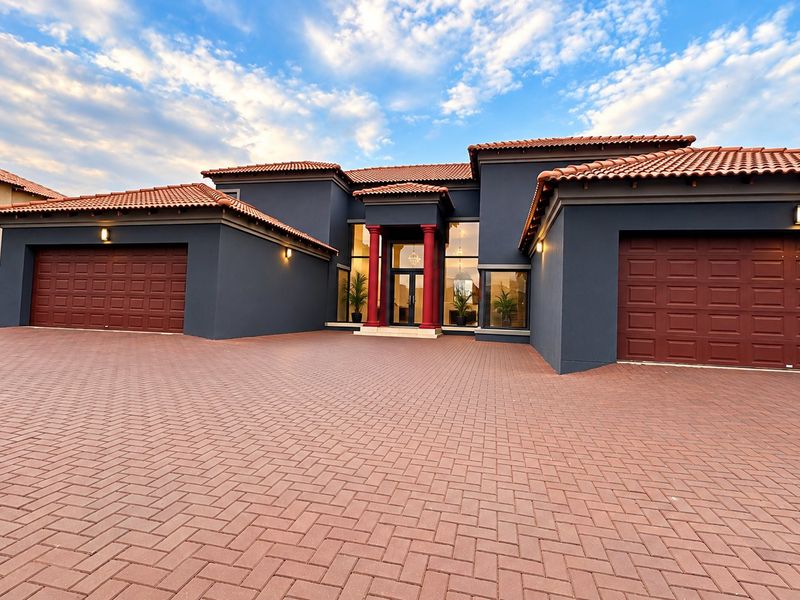Modern luxury residence featuring a striking dark facade, terracotta roof tiles, double garages, and a grand entrance with decorative columns and extensive paving.