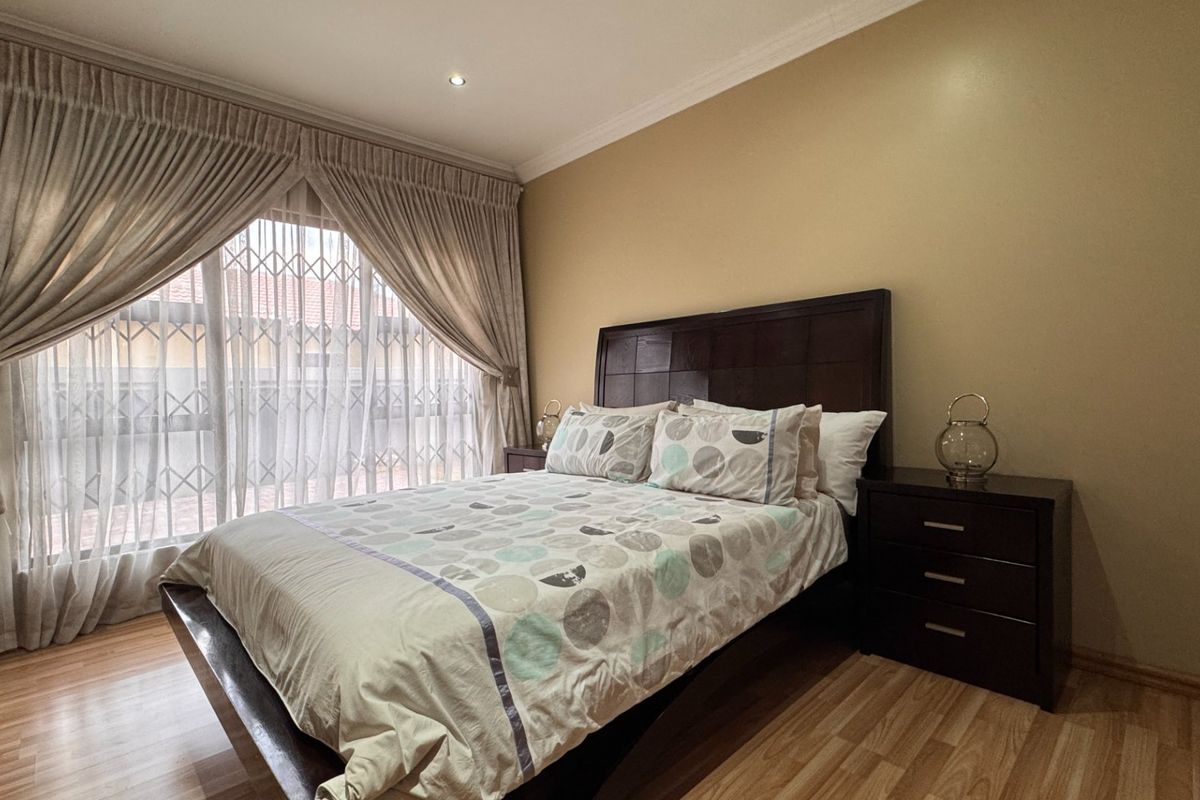 A well-maintained bedroom featuring laminate flooring, recessed lighting, and a sliding door with an integrated security gate.