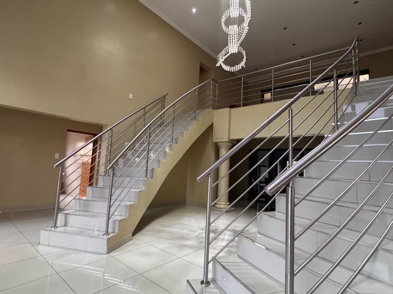 Spacious grand entrance hall featuring a double staircase with stainless steel balustrades, tiled flooring, and a modern feature chandelier.