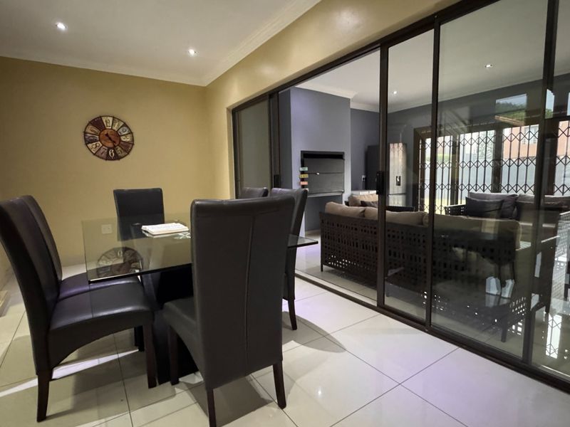 A bright dining area featuring tiled floors and recessed lighting, with large sliding glass doors opening onto an outdoor patio space with a built-in fireplace.