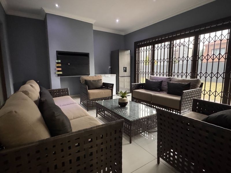 A spacious covered patio featuring tiled flooring, recessed downlights, and a built-in braai, providing a comfortable area for outdoor entertaining.