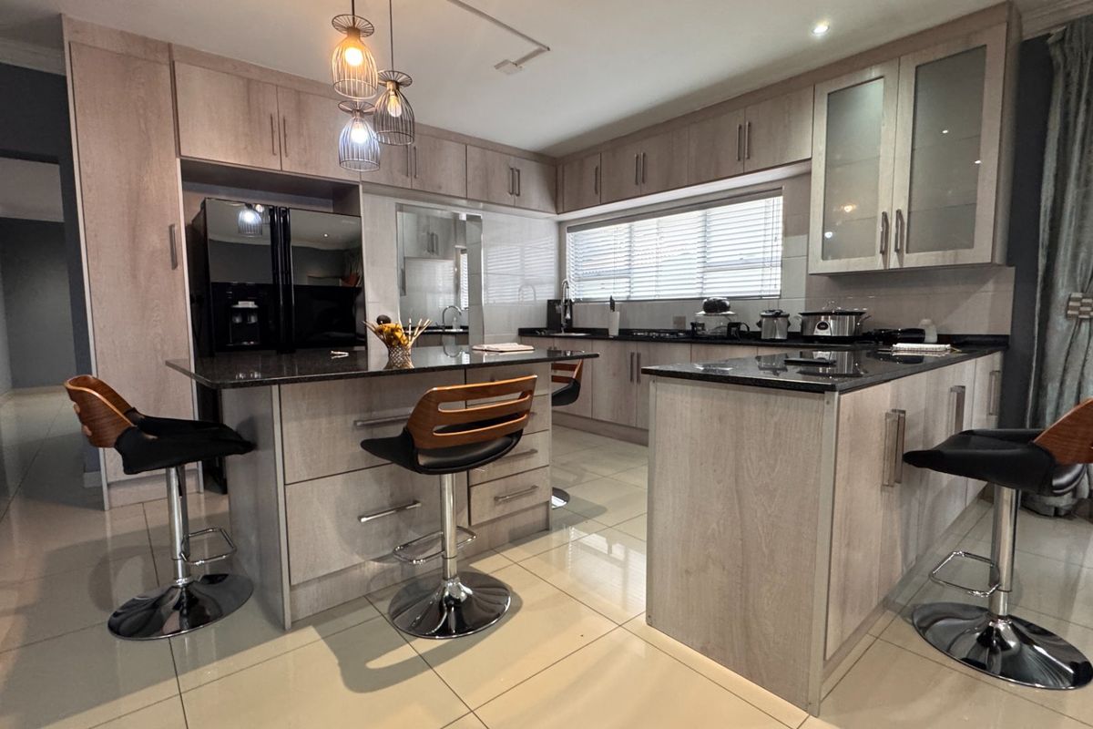 Modern kitchen featuring light wood cabinetry, granite countertops, a central island with breakfast bar seating, and tiled flooring.
