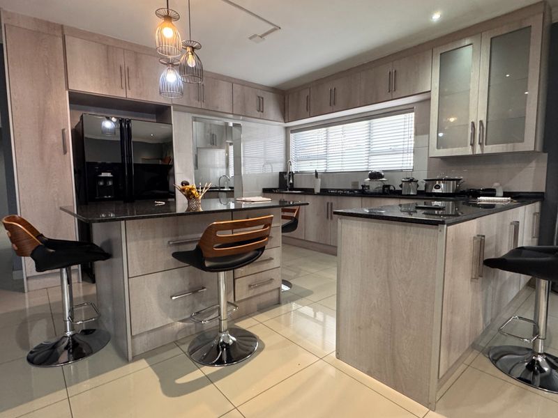 Modern kitchen featuring light wood cabinetry, granite countertops, a central island with breakfast bar seating, and tiled flooring.
