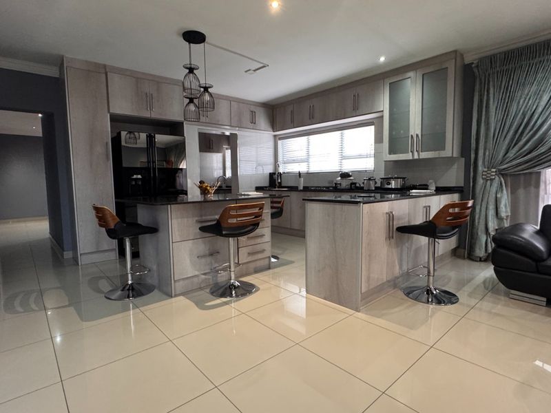Modern open-plan kitchen featuring light wood-finish cabinetry, granite countertops, a central island, and polished porcelain floor tiles.