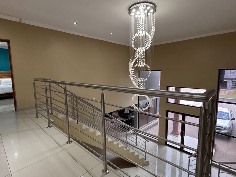Spacious upper-level landing featuring polished tile flooring, a modern stainless steel balustrade, and an impressive contemporary crystal chandelier.