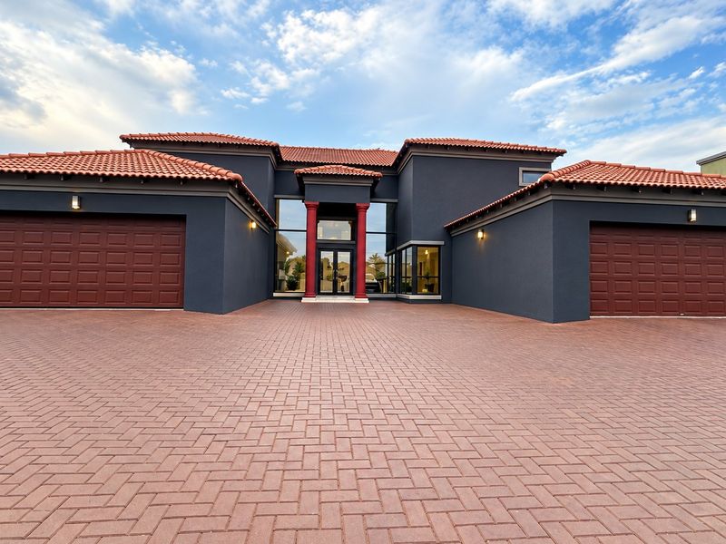 Modern double-story residence featuring a spacious paved driveway, double garages, and a striking double-volume entrance with decorative columns and terracotta roof tiles.