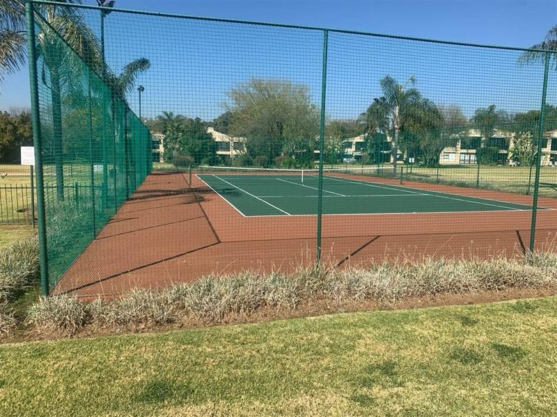 A well-maintained outdoor tennis court featuring a hard surface, perimeter safety netting, and integrated floodlighting within the residential complex.