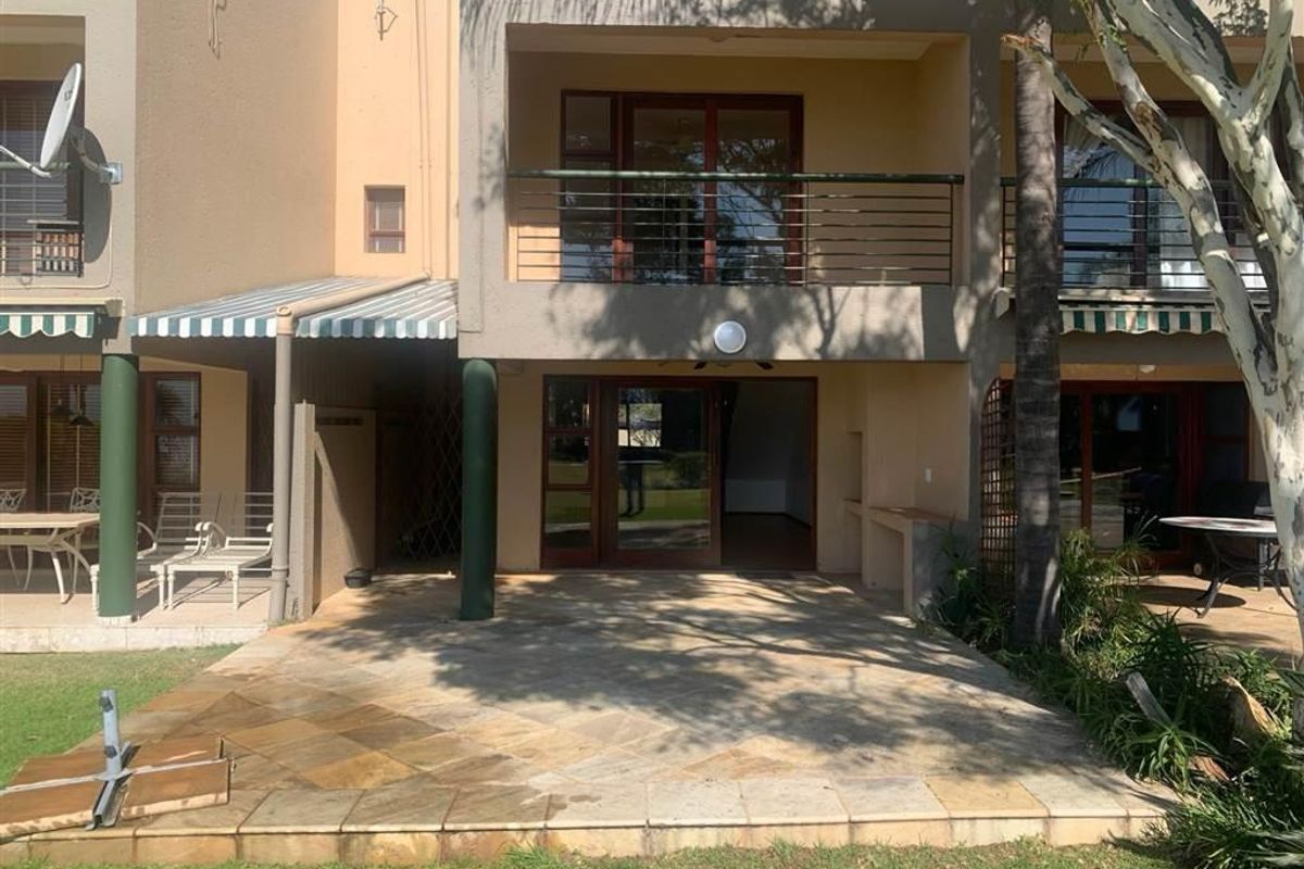 Rear view of the townhouse featuring a stone-paved patio, built-in braai area, and an upper-level balcony with metal railings.