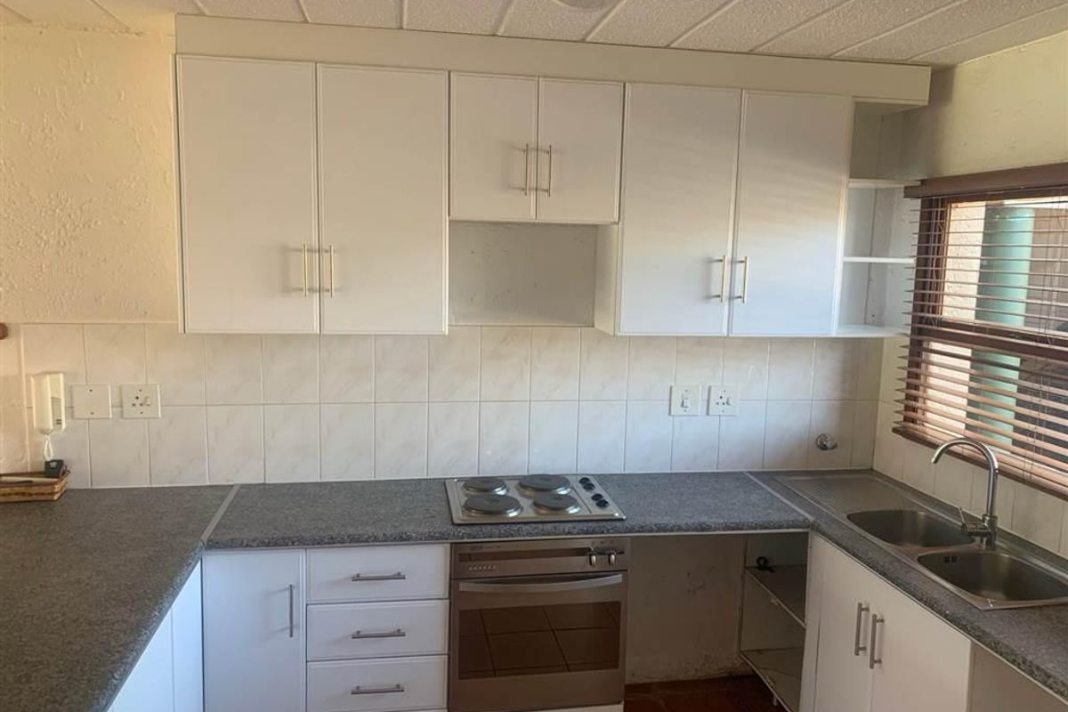 A functional kitchen featuring white cabinetry, laminate countertops, an integrated electric hob and oven, and a stainless steel double sink with tiled backsplash.