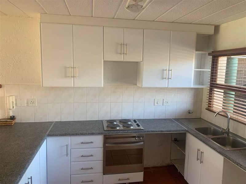 A functional kitchen featuring white cabinetry, laminate countertops, an integrated electric hob and oven, and a stainless steel double sink with tiled backsplash.