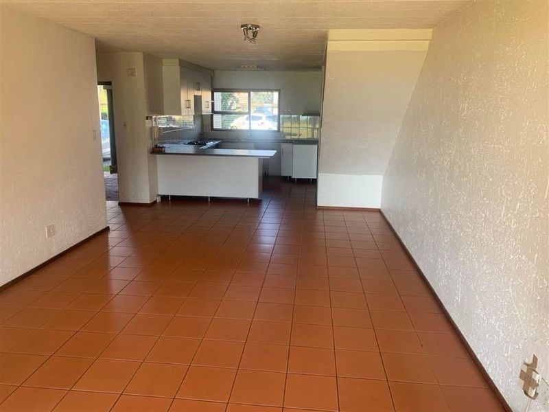 An open-plan living and kitchen area featuring tiled flooring, built-in kitchen cabinetry, and a staircase, offering a blank canvas for renovation.