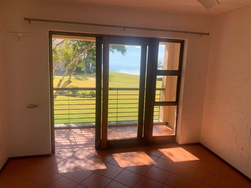 An empty living room featuring terracotta floor tiles and large sliding glass doors that open onto a balcony with scenic views.