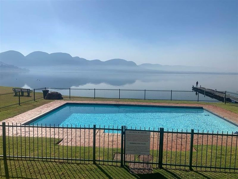 A well-maintained swimming pool area featuring brick paving and metal fencing, offering scenic views of the lake and mountains.