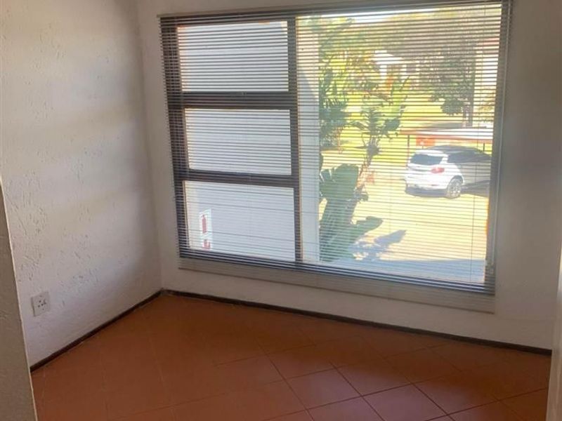 An empty bedroom featuring tiled flooring, a ceiling fan, and large windows with venetian blinds, offering a blank canvas for potential updates.