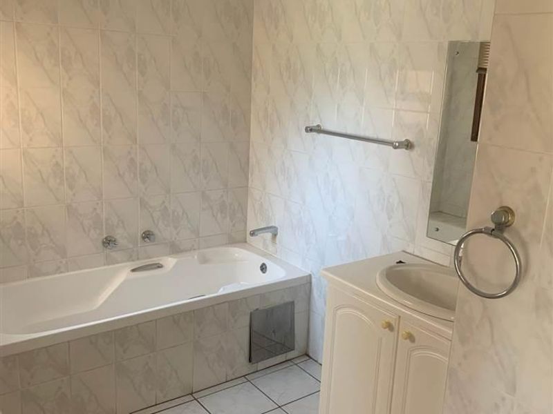A functional bathroom featuring a built-in bathtub, vanity cabinet with integrated sink, and full-height wall tiling.