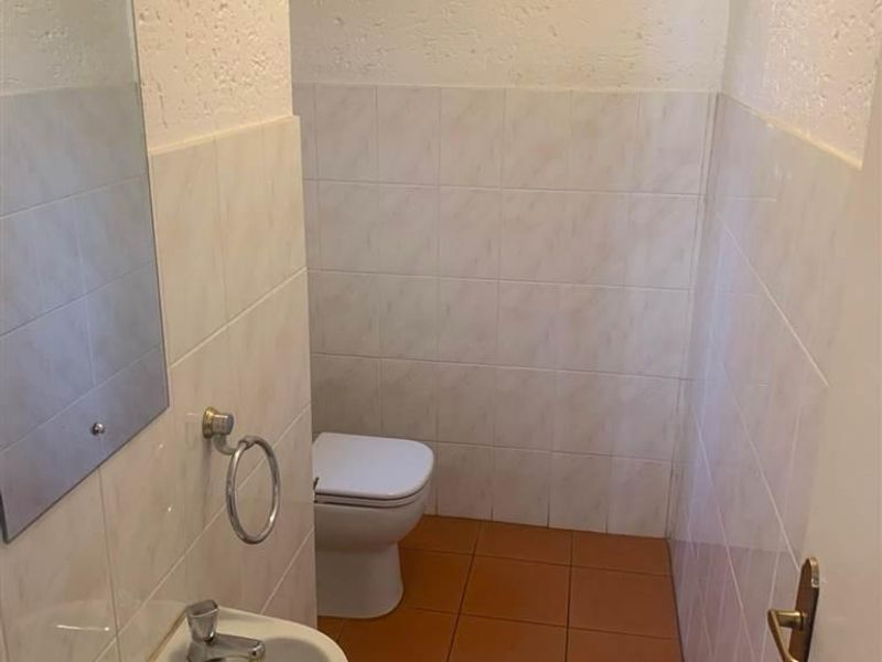 A compact guest bathroom featuring a pedestal basin, toilet, and neutral wall and floor tiling, presenting a dated but functional space.