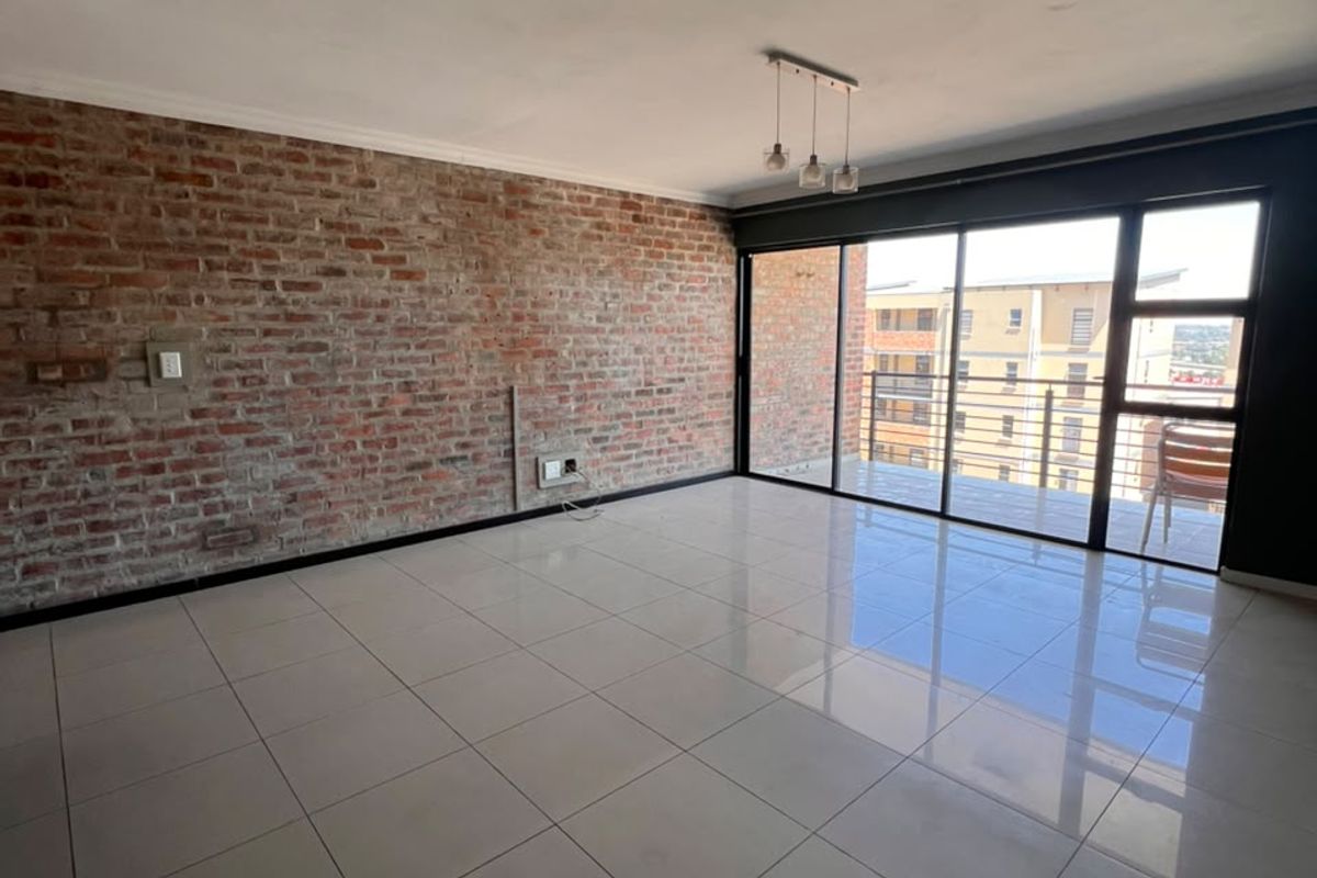 Spacious living area featuring an exposed brick accent wall, polished tile flooring, and large sliding glass doors leading to a balcony.