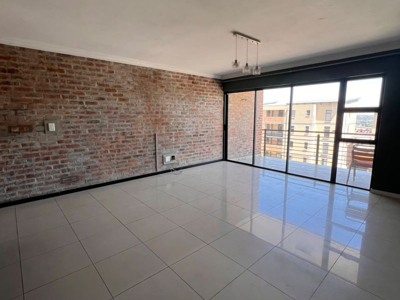 Spacious living area featuring an exposed brick accent wall, polished tile flooring, and large sliding glass doors leading to a balcony.