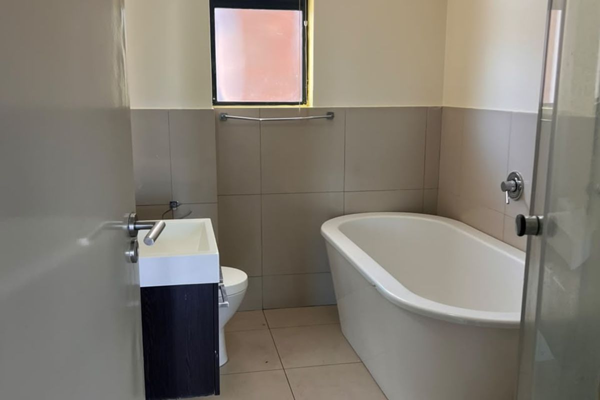 A clean, modern bathroom featuring a freestanding bathtub, a vanity with basin, a toilet, and a separate shower enclosure with neutral floor and wall tiles.