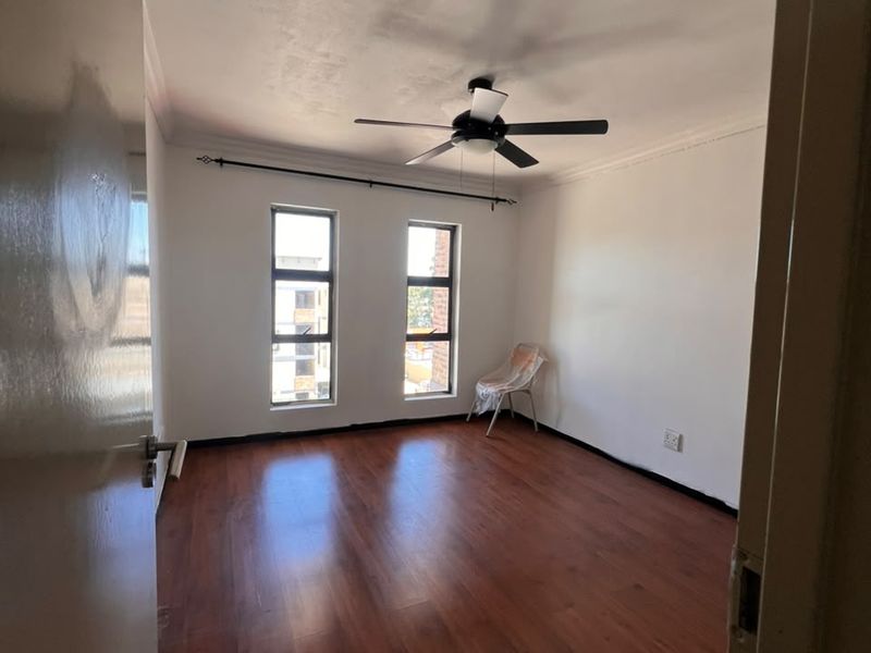 A vacant bedroom featuring laminate flooring, a ceiling fan, and dual windows, offering a blank canvas for personalization.