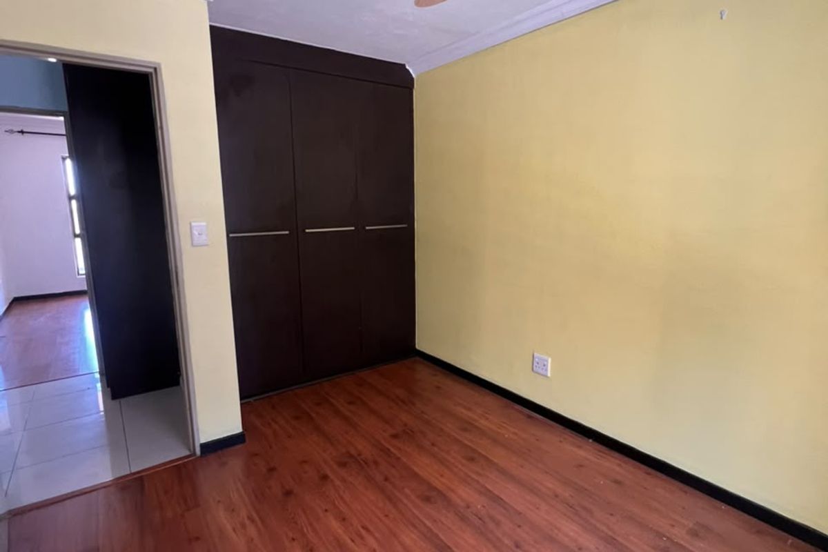 An empty bedroom featuring laminate flooring, built-in dark wood cupboards, and a ceiling fan, offering a clean canvas for personalization.