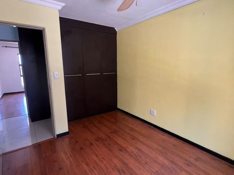 An empty bedroom featuring laminate flooring, built-in dark wood cupboards, and a ceiling fan, offering a clean canvas for personalization.