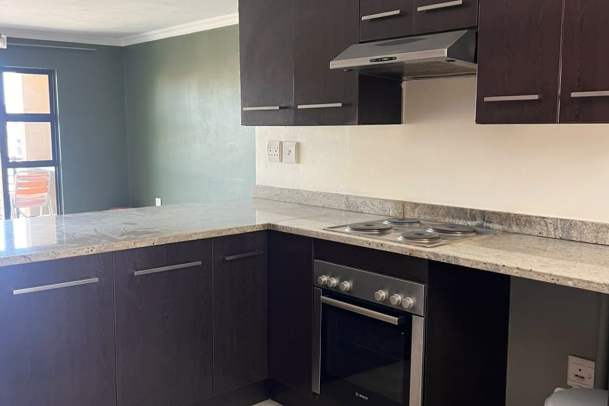 A functional kitchen featuring dark wood cabinetry, granite countertops, and built-in appliances, including an oven and hob, with tiled flooring throughout.