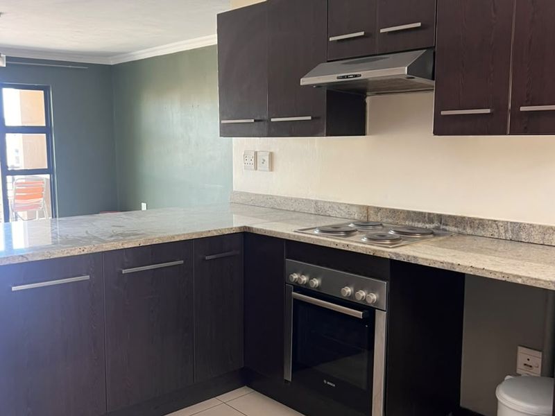 A functional kitchen featuring dark wood cabinetry, granite countertops, and built-in appliances, including an oven and hob, with tiled flooring throughout.