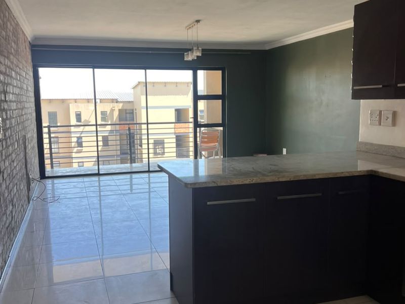 Open-plan living area featuring a kitchen with granite countertops, dark cabinetry, tiled floors, and an exposed brick wall leading to a balcony.