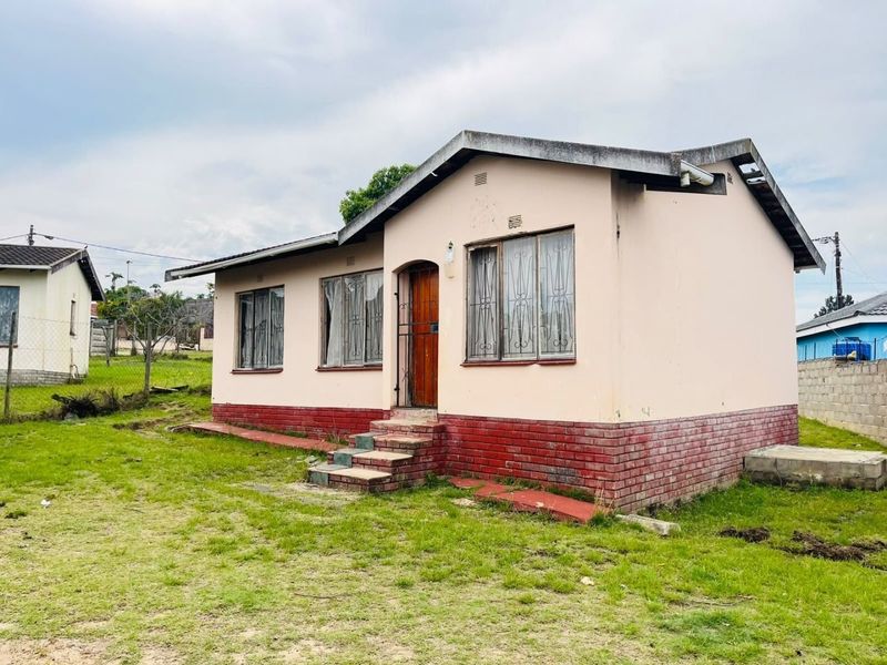 A detached single-story house featuring a brick plinth, metal window frames, and a pitched roof, situated on a grassed plot.