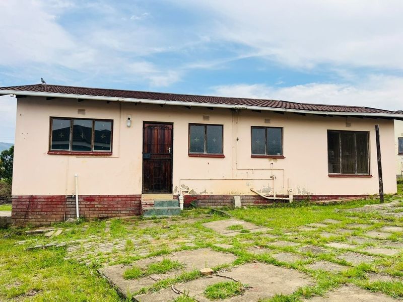 Rear exterior view of a single-story house featuring a tiled roof, brick base, and paved yard area requiring maintenance and cosmetic updates.