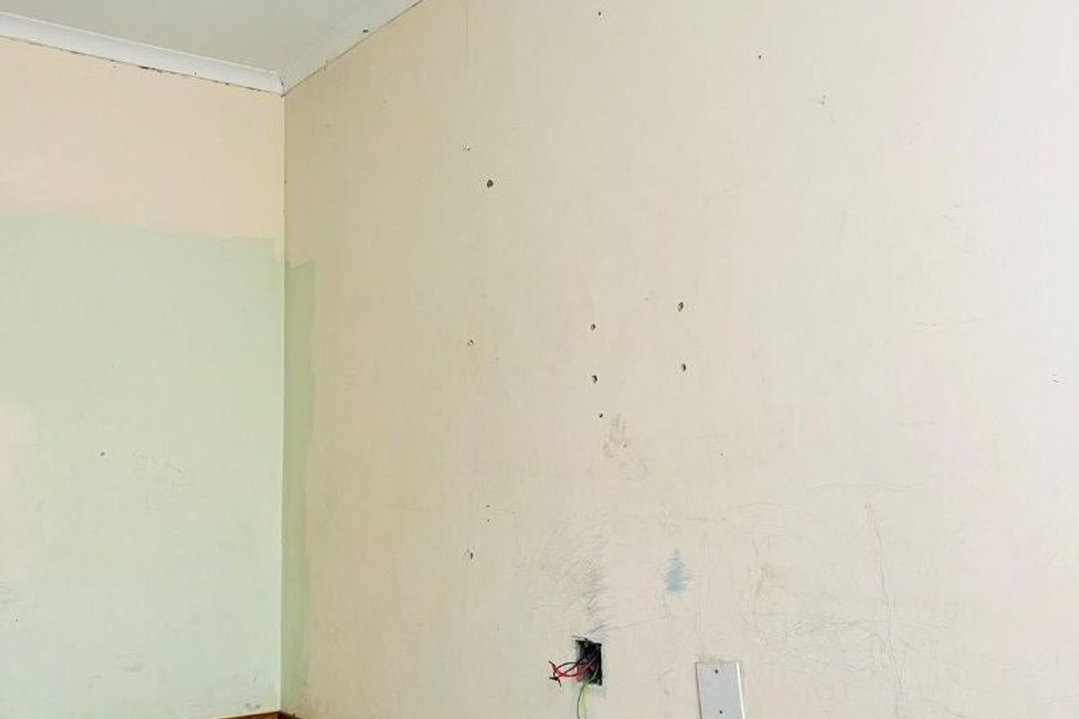 An empty bedroom featuring dark tiled flooring, a ceiling fan, and walls requiring cosmetic repair and repainting.
