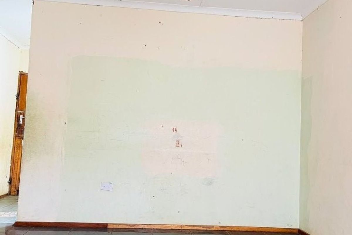 An empty living room featuring dark tiled flooring, a ceiling fan, and walls requiring cosmetic repair and repainting.