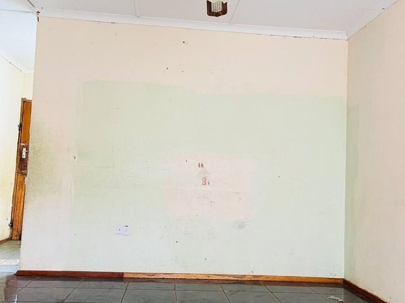 An empty living room featuring dark tiled flooring, a ceiling fan, and walls requiring cosmetic repair and repainting.