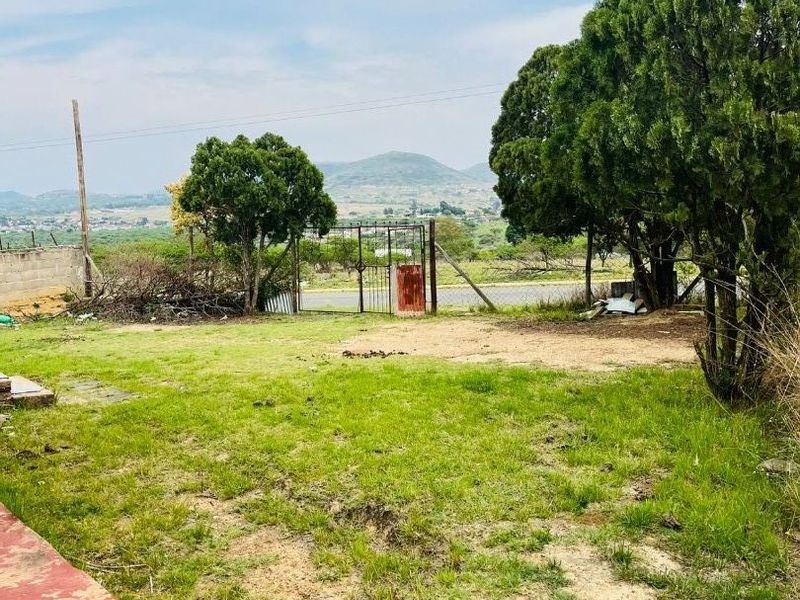 A spacious outdoor garden area featuring a metal gate, perimeter fencing, and scenic mountain views in the background.