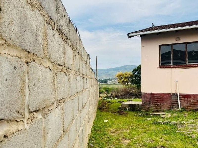 Rear exterior view showing a concrete block boundary wall with barbed wire, a tiled roof structure, and a grassed backyard area.