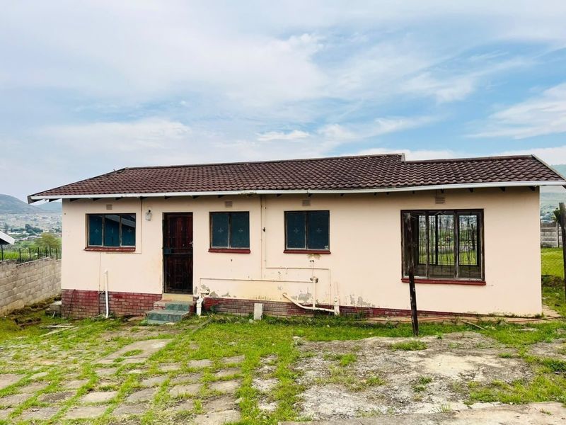 Rear view of a single-story house featuring a tiled roof, security bars, and a paved yard area in need of exterior maintenance and painting.