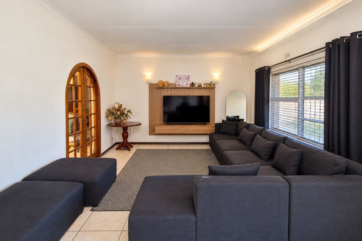 A well-maintained living room featuring tiled floors, cove lighting, a built-in media console, and an elegant arched double-door entrance.