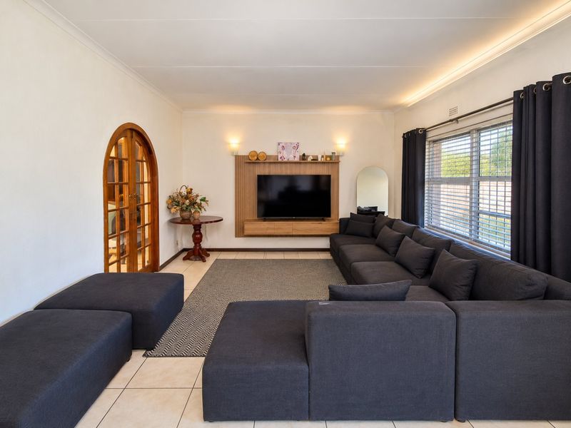 A well-maintained living room featuring tiled floors, cove lighting, a built-in media console, and an elegant arched double-door entrance.